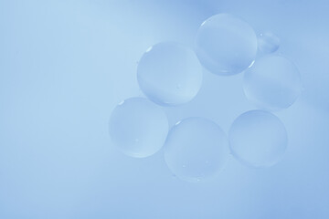 Macro photography of transparent oil bubbles clustered together on a soft blue background, creating a serene and minimal composition