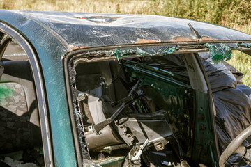 Car with a smashed windshield and a black bag on the back seat. Scene is one of destruction and chaos