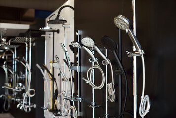 Obraz premium Assortment of new shower heads in a plumbing store, close-up. Variety of modern chrome and silver metal shower heads on black background. Wholesale and retail plumbing trade, exhibition