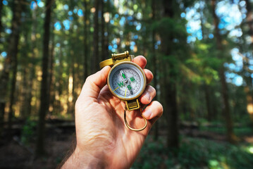 Naklejka premium A man's hand holds a compass against a background of trees, navigating in the forest