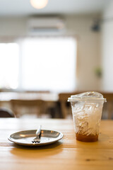 A glass of black coffee and ice with a little left placed together with empty dessert dish after eating on wood table at cafe
