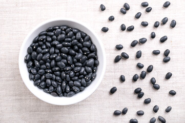 Black beans, in a white bowl, on linen. Dried variety of common beans, Phaseolus vulgaris, also known as black turtle beans, and caviar criollo. Type of bean with satiny black skin and white center.