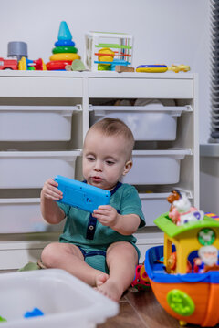 A small baby is happily sitting on the floor and playing with a toy phone
