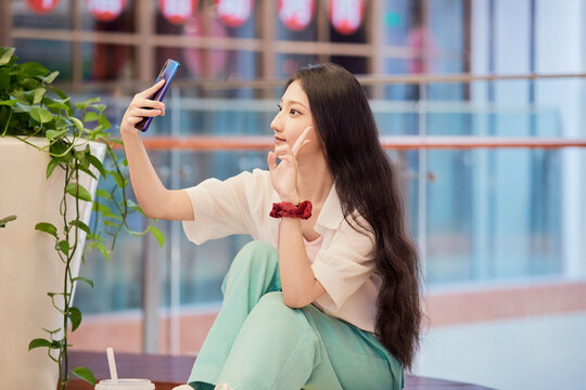 Chinese girl taking selfies with her phone in a shopping mall rest area on a holiday