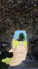 Obraz premium Natural landscape of the sea seen through a large wall opening, showing blue sky, greenery, and serene ocean view.