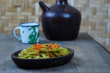 Tumis pare or Indonesian stir-fried bitter melon with chili peppers, served on a rustic wooden table. The dish has a vibrant mix of green and red colors.