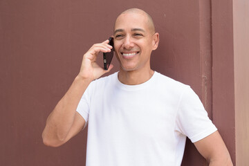 Studio style portrait of bald Hispanic man using mobile phone