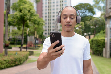 Latin bald man using phone while walking in city, digital lifestyle and active wellness concept