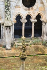 Obraz premium A moss-covered stone cross stands prominently in the foreground, overlooking the ancient cloister of Bom Jesus do Monte in Braga. Sunlight filters through arches