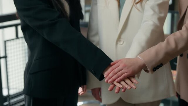 Three happy candid business women success teamwork in office stacking hands multiracial colleagues multiethnic businesswomen girls females partnership corporate celebrating Caucasian Asian ladies