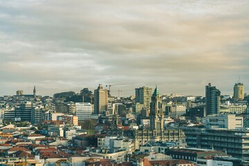 An expansive view of Porto reveals its architecture and skyline under a cloudy sky. Buildings of varying heights intermingle with historic churches
