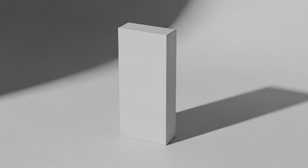 Fototapeta premium A blank white rectangular product box stands upright on a clean light surface with sharp, minimalist shadows, ideal for branding or packaging design mockups.