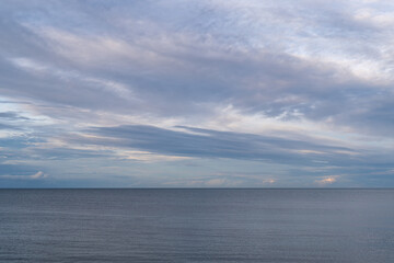 Fototapeta premium Calm ocean waters under a cloudy sky at dusk near the shoreline