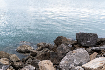 Calm water meets rugged rocks along the shore at a scenic lakeside location during the late afternoon light