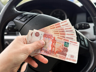 The five thousand dollar bills in the hands of a man sitting in car he bought. A man with Russian money in his hand. Insurance, loan concept. Deal of buy, rent new car. A wad of money in a man's hand.