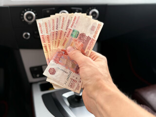 The five thousand dollar bills in the hands of a man sitting in car he bought. A man with Russian money in his hand. Insurance, loan concept. Deal of buy, rent new car. A wad of money in a man's hand.