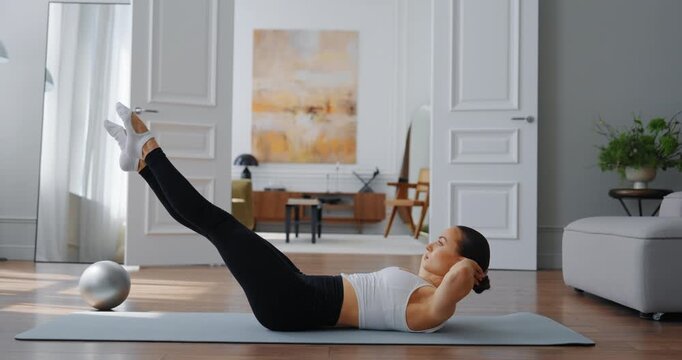 Female athlete performing leg raises on exercise mat in modern living room with natural light