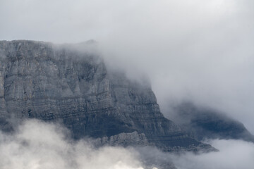 Prominent rocky mountain surrounded by clouds and mist creating a rugged and mysterious setting