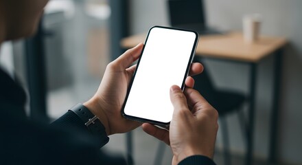Close-up of a man's hands holding a smartphone with a blank white screen in a modern office setting