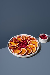 Rodajas de naranja sanguina y semillas de granada en un plato blanco sobre un fondo azul	