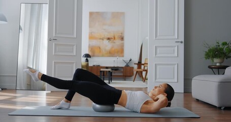 Fit woman performing core exercises on stability ball in modern living room with natural light - Powered by Adobe