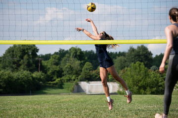 Volleyball player reaching high to pass a ball during grass doubles game