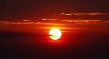 Dramatic sunrise over a dark horizon with clouds and a vibrant sun
