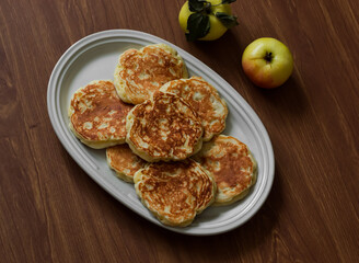 Apple fritters on an oval plate on a wooden table, top view
