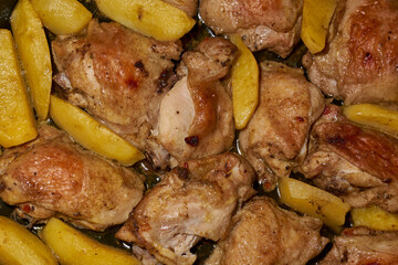 Oven-baked chicken pieces with potato slices and seasoning mixture. Close-up.