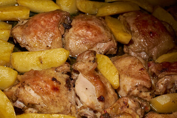 Oven-baked chicken pieces with potato slices and seasoning mixture. Close-up.