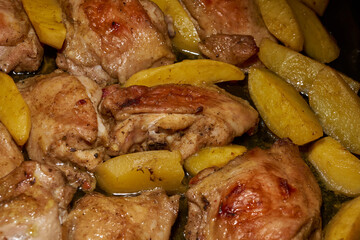 Oven-baked chicken pieces with potato slices and seasoning mixture. Close-up.