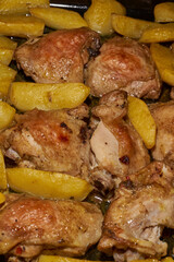 Oven-baked chicken pieces with potato slices and seasoning mixture. Close-up.