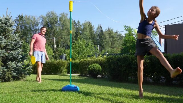 Father and daughter play tetherball in their sunny backyard, enjoying summer fun and togetherness