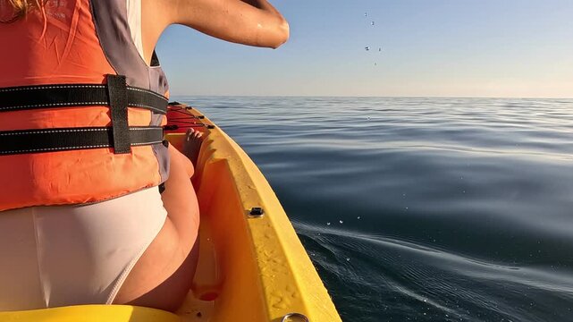 Kayak paddling ocean, woman on yellow kayak on calm sea on a peaceful morning