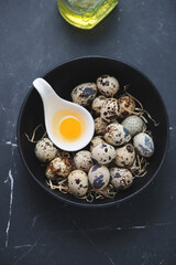 Bowl with raw uncooked quail eggs on a black marble background, vertical shot
