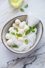 Bowl with freshly made mini mozzarella cheese and basil on a white granite background, vertical shot, elevated view