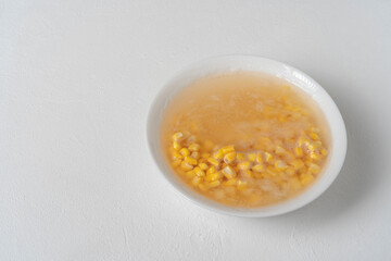 Yellow corn soaking in a white bowl. On a white table.