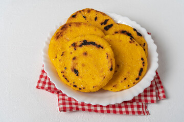 Arepas made from threshed yellow corn. On a white plate. On a white table. With a red and white cloth napkin.