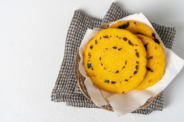 Arepas made of threshed yellow corn in a wicker basket on a white table, with a white paper napkin and a gray cloth napkin.