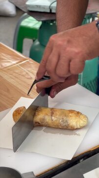 South Asian Thai man slices banana roti with a knife at a Thai food market