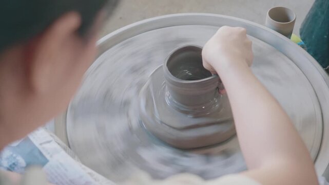 A close-up of hands skillfully shaping clay on a pottery wheel. The artist's focus highlights the intricate process of creating pottery, showcasing a blend of tradition and artistry in ceramic craftsm