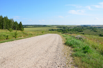 Scenic gravel road leading through a lush countryside under a bright blue sky to the village