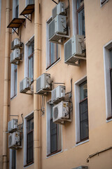 Facade of building with many air conditioners on windows in southern hot country. Yellow house exterior on city street. Escape from heat, creating favorable microclimate in urban apartments concept.