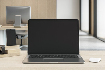 Fototapeta premium Blank black laptop screen mockup on wooden desk in modern office with desktop and smartphone in background during daylight hours. 3D Rendering