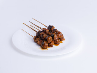 Grilled Indonesian meatball satay with spicy peanut sauce on a white plate. Concepts for Asian street food, traditional, grilled, snack, savory, spicy, isolated.
