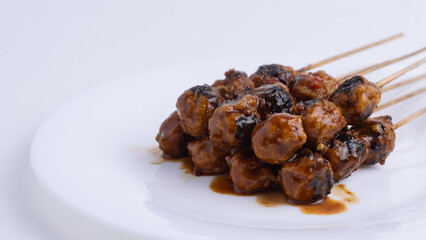 A close up of grilled meatball satay with spicy peanut sauce on a white plate with copy space. Concepts for Indonesian food, street food, traditional, grilled, snack, savory, spicy.

