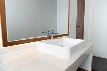 Minimalist bathroom interior with modern white sink, chrome faucet, large mirror framed in wood. Bright lighting and clean design ideal for home decor, hygiene, hospitality, and real estate concept.