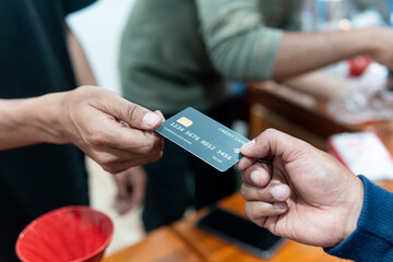 Close-up of a hand giving a black dummy credit card to another hand at a cafe counter, with a blurred barista in the background. Perfect for finance, payment, shopping, and cafe business concepts.