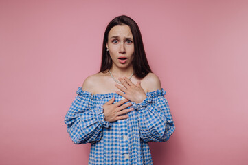 Obraz premium A surprised woman in a blue checkered off-shoulder dress against a pink background.