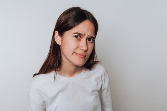 A young woman with long brown hair wearing a white shirt, expressing skepticism. - Powered by Adobe